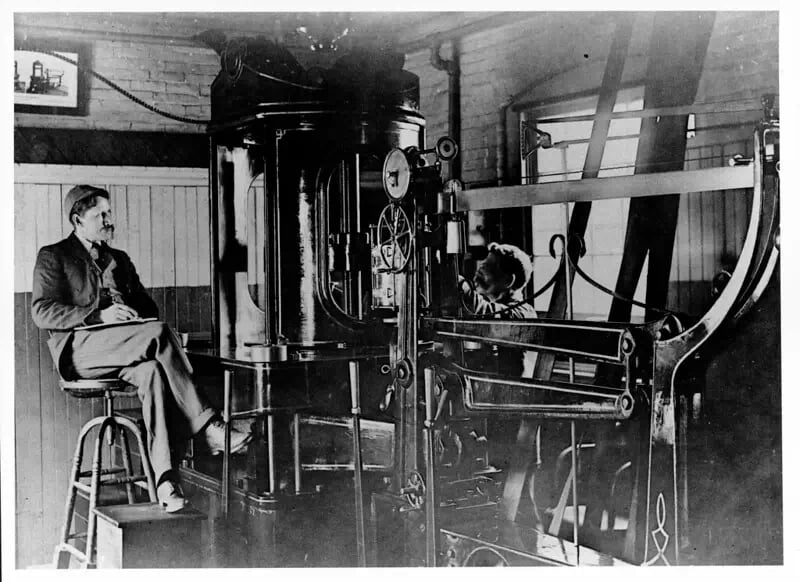 Foto de 1885. Um homem, possivelmente Frederick Taylor, observa um engenheiro trabalhando na Midvale Steel Company, na Filadélfia. Kheel Center CC BY 2.0.